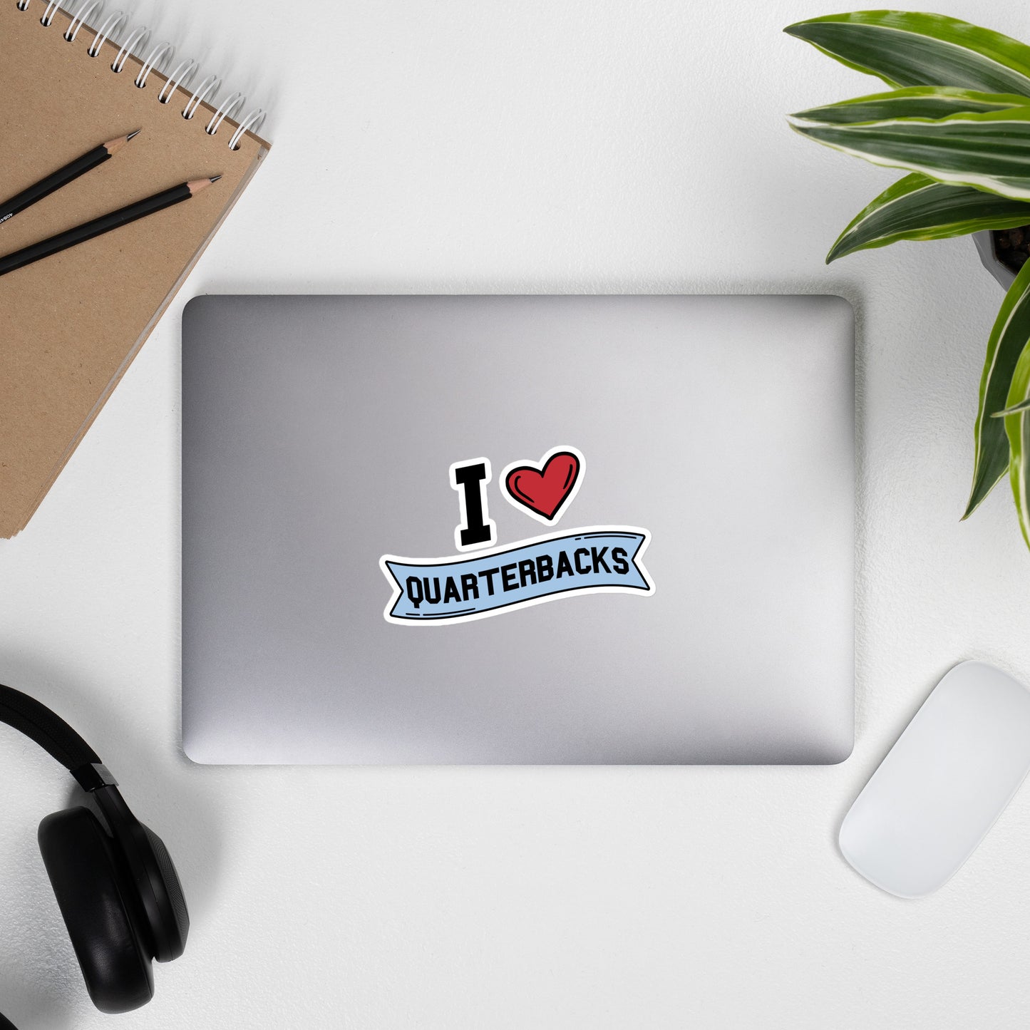 A sticker that reads "I Heart Quarterbacks" with a large red heart, Quarterbacks is printed on a blue banner. The sticker is 5.5 x 5.5 inches