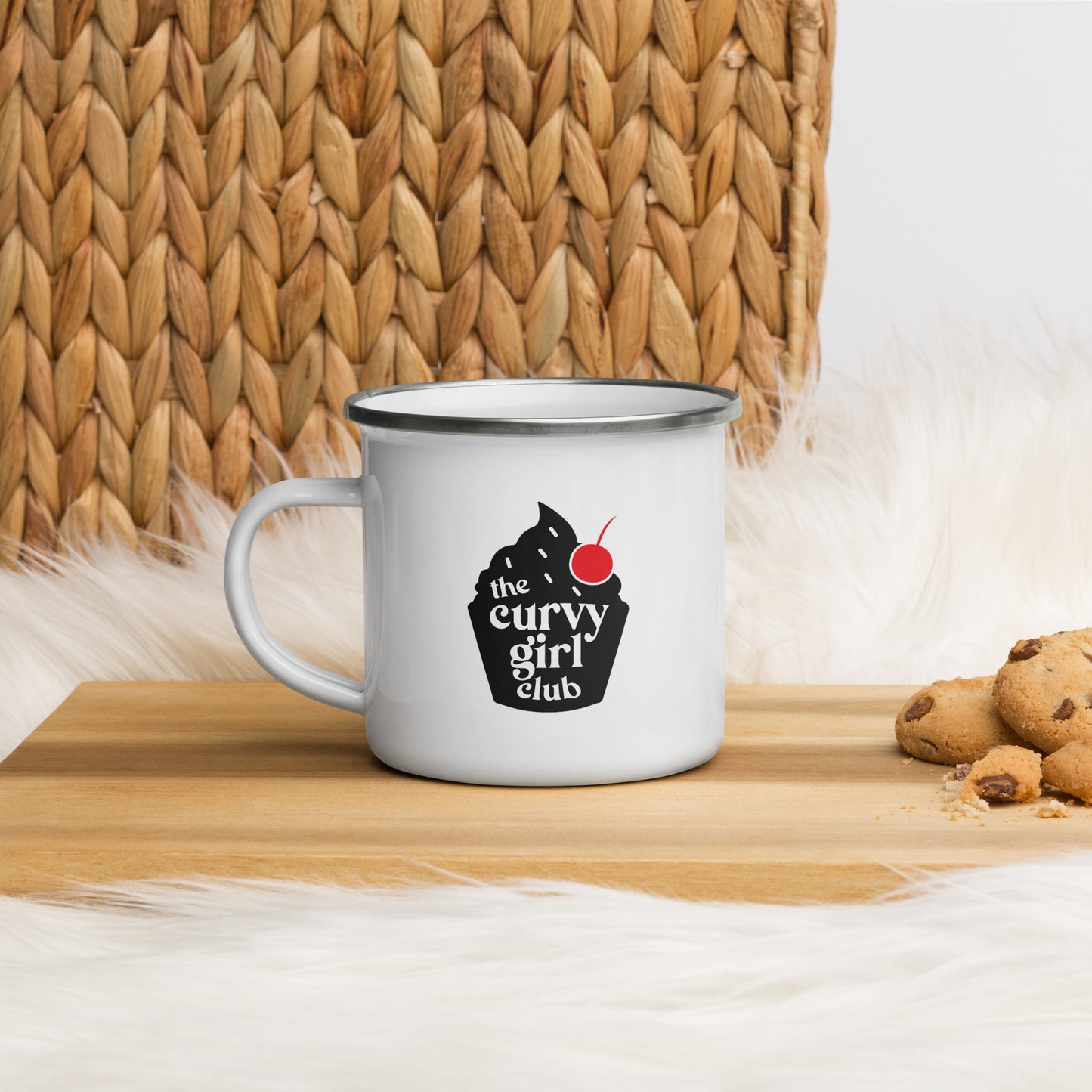 a white enamel mug with a cupcake design. The cupcake design is black, with a red cherry. Inside the cupcake are the words the Curvy Girl Club