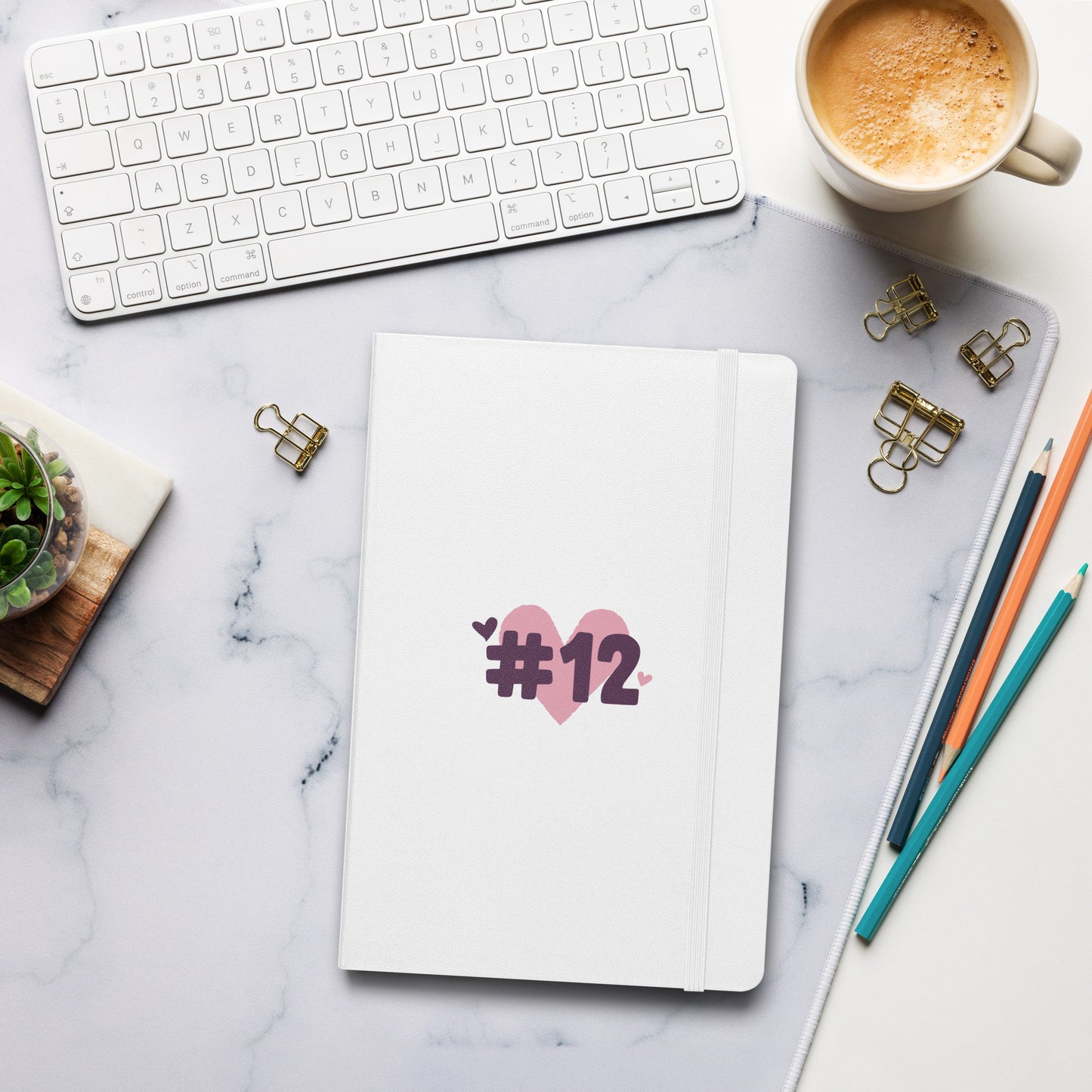 a hardcover notebook with the I Heart #12 Logo. The Number 12 Logo is a large pink heart with #12 in black written over the heart.