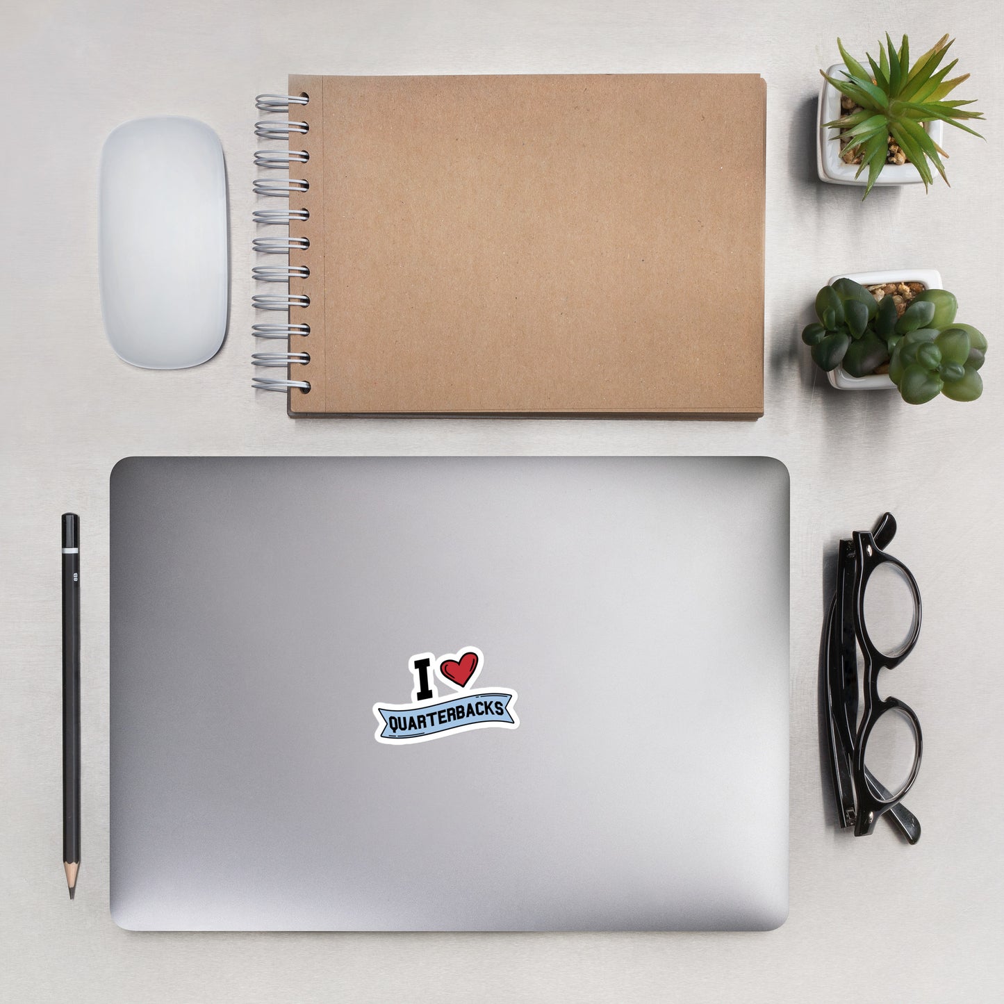A sticker that reads "I Heart Quarterbacks" with a large red heart, Quarterbacks is printed on a blue banner. The sticker is 3 x 3 inches