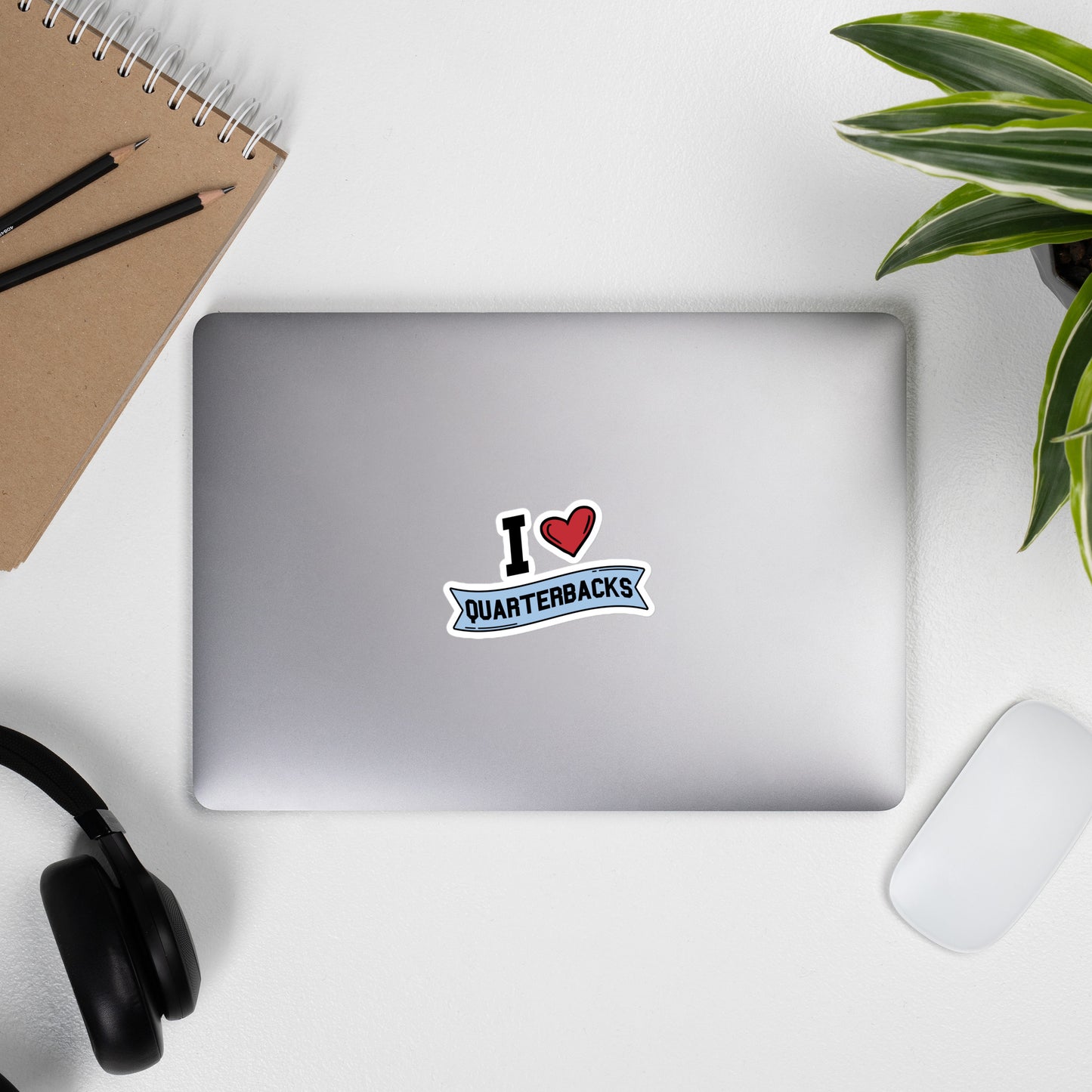 A sticker that reads "I Heart Quarterbacks" with a large red heart, Quarterbacks is printed on a blue banner. The sticker is 4 x 4 inches