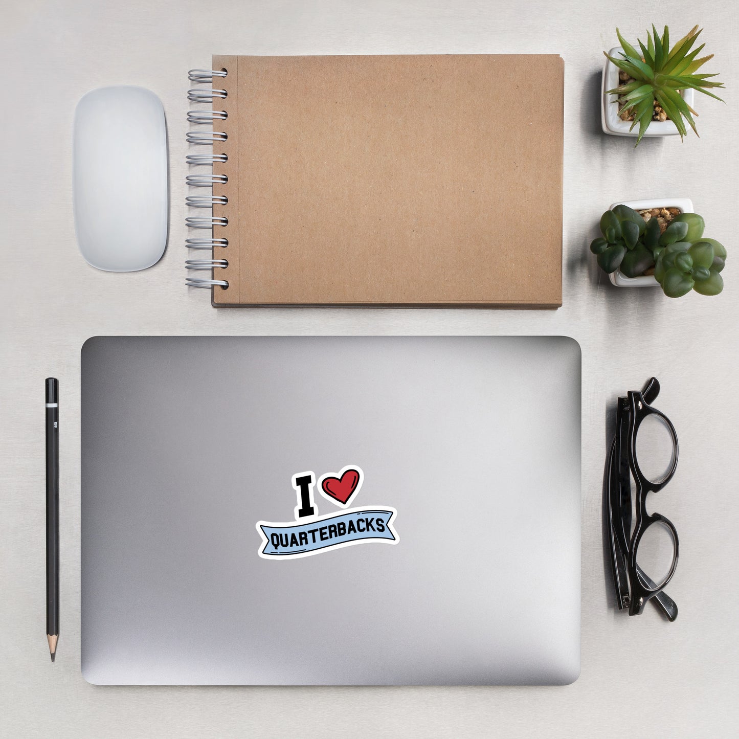 A sticker that reads "I Heart Quarterbacks" with a large red heart, Quarterbacks is printed on a blue banner. The sticker is 4 x 4 inches
