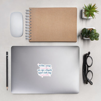 A sticker with blue and pink text, a combination of print and cursive that reads "Write Your Number on my cheek and call me cupcake". The sticker is 4 x 4 inches