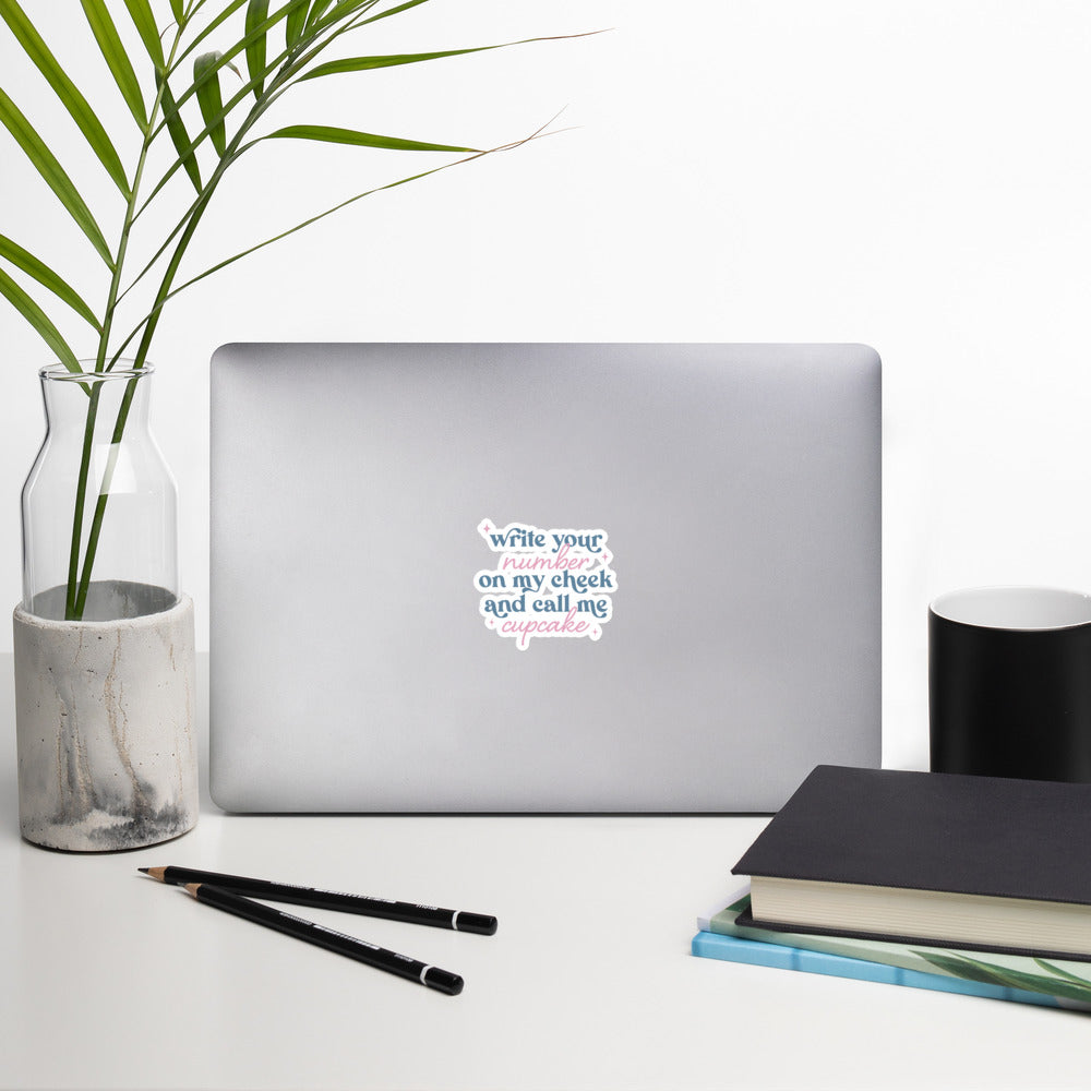 A sticker with blue and pink text, a combination of print and cursive that reads "Write Your Number on my cheek and call me cupcake". The sticker is 4 x 4 inches