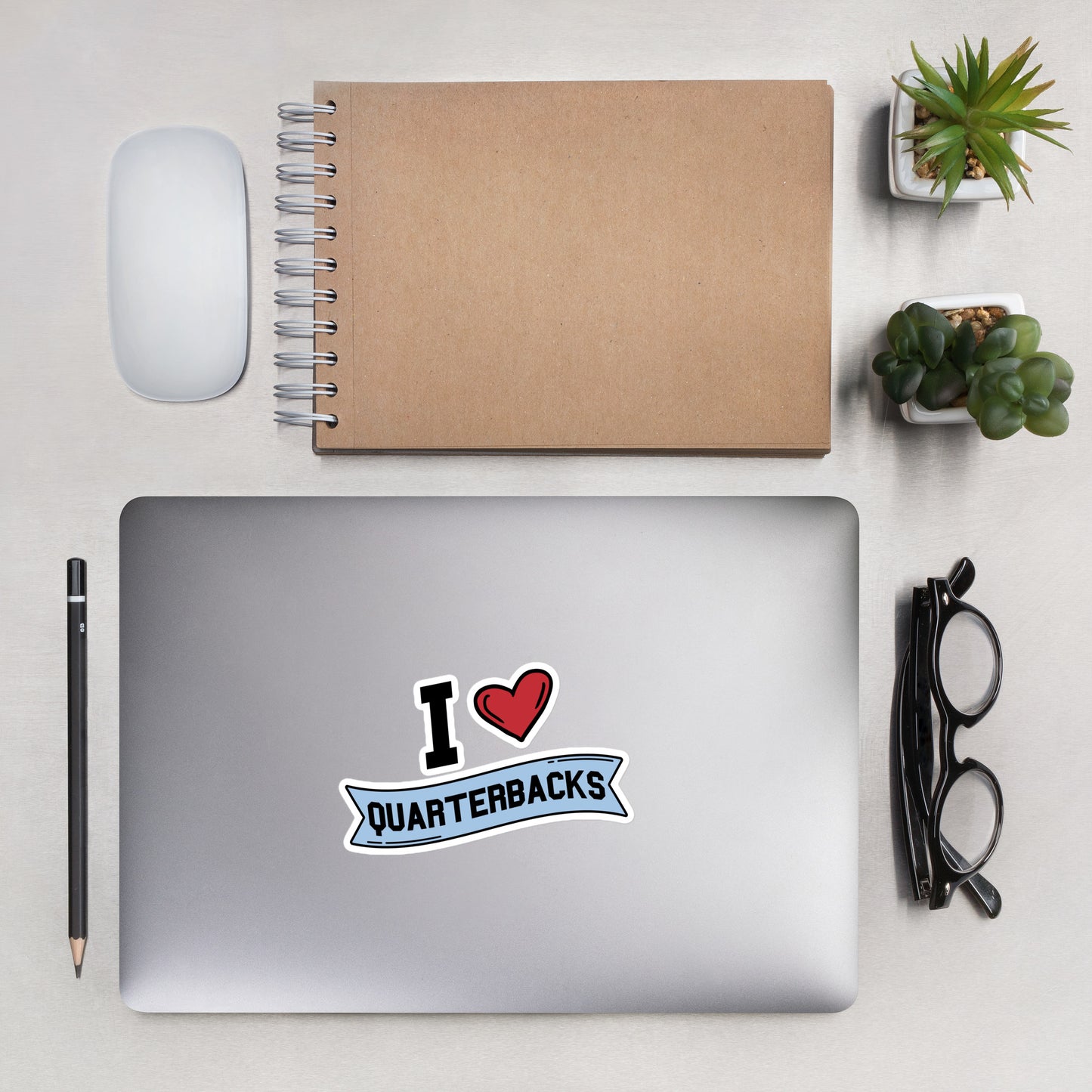 A sticker that reads "I Heart Quarterbacks" with a large red heart, Quarterbacks is printed on a blue banner. The sticker is 5.5 x 5.5 inches
