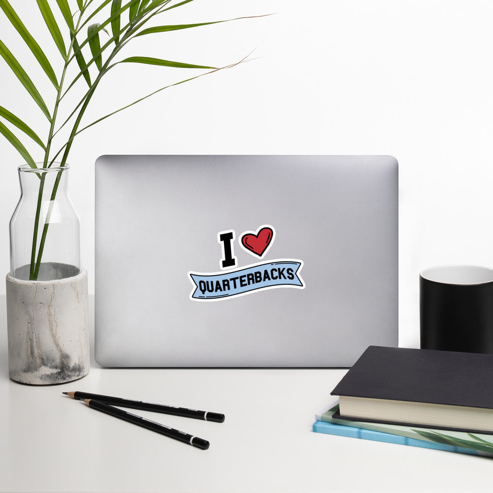 A sticker that reads "I Heart Quarterbacks" with a large red heart, Quarterbacks is printed on a blue banner. The sticker is 5.5 x 5.5 inches
