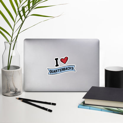 A sticker that reads "I Heart Quarterbacks" with a large red heart, Quarterbacks is printed on a blue banner. The sticker is 5.5 x 5.5 inches