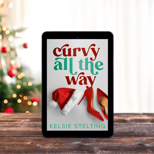 An ebook cover sits on a table, with christmas lights behind it. The book is titled Curvy All the Way by Kelsie Stelting and features a santa hat and red heels on the cover