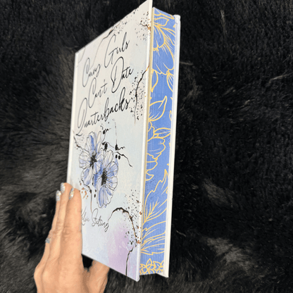 a special edition hardcover of Curvy Girls Can't Date Quarterbacks by Kelsie Stelting, tilted at an angle to show the pages are painted blue with gold designs 