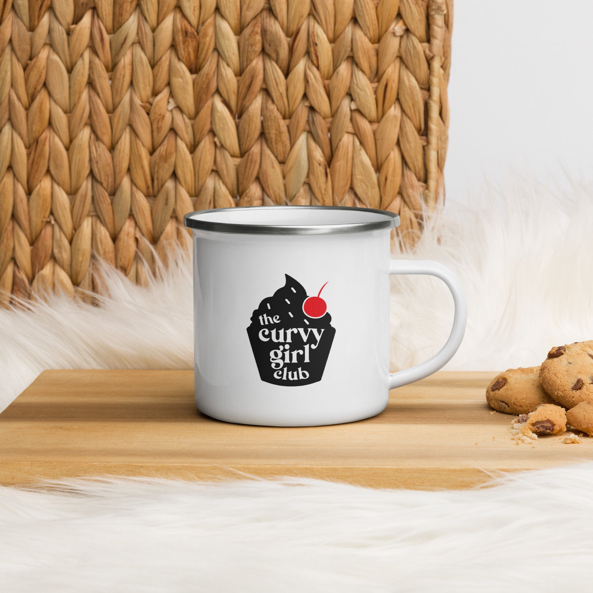a white enamel mug with the Curvy Girl Cupcake design. The cupcake design is black, with a red cherry. Inside the cupcake are the words the Curvy Girl Club