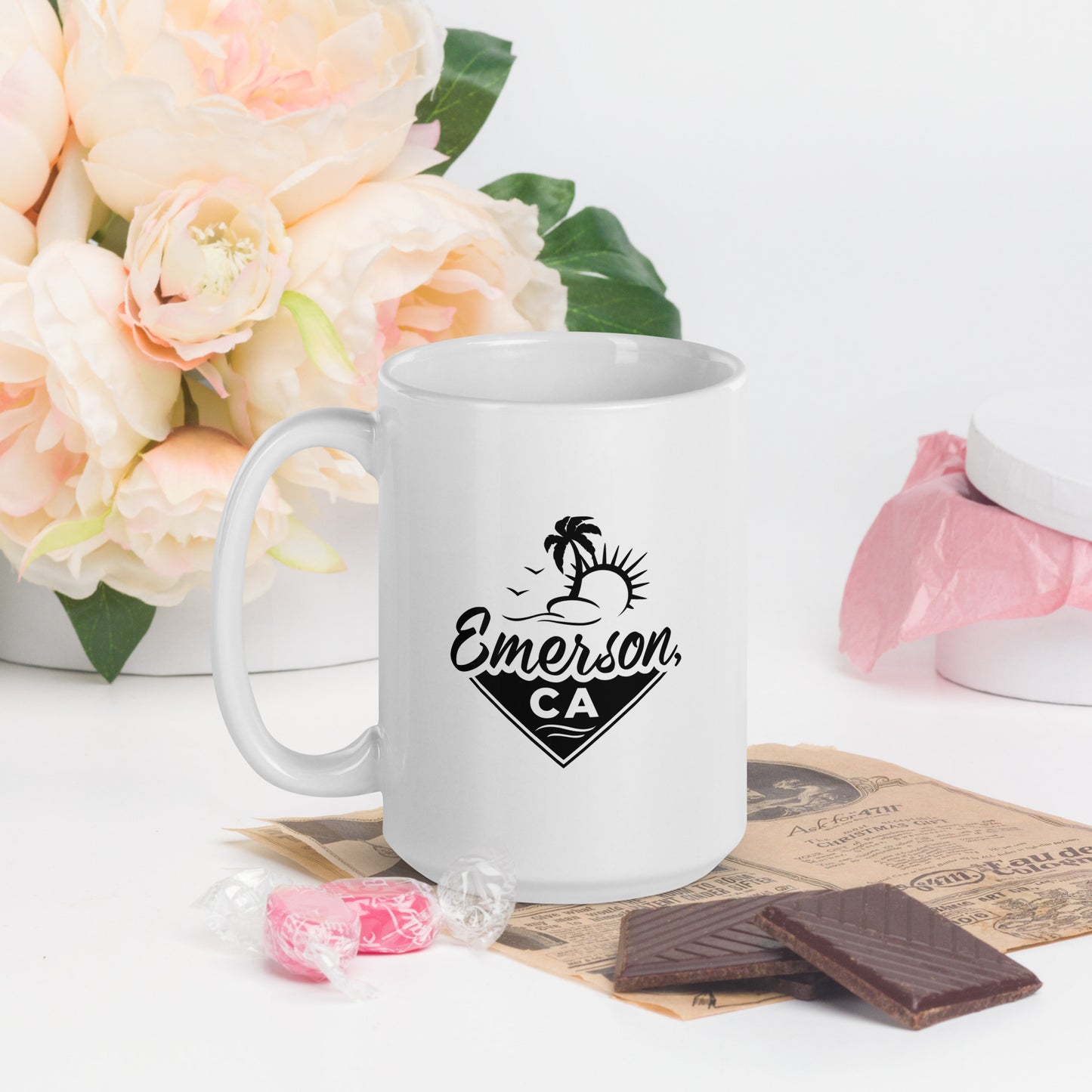 A white mug with the Emerson, CA logo. Preeminently featuring a beach, a palm tree and the sun