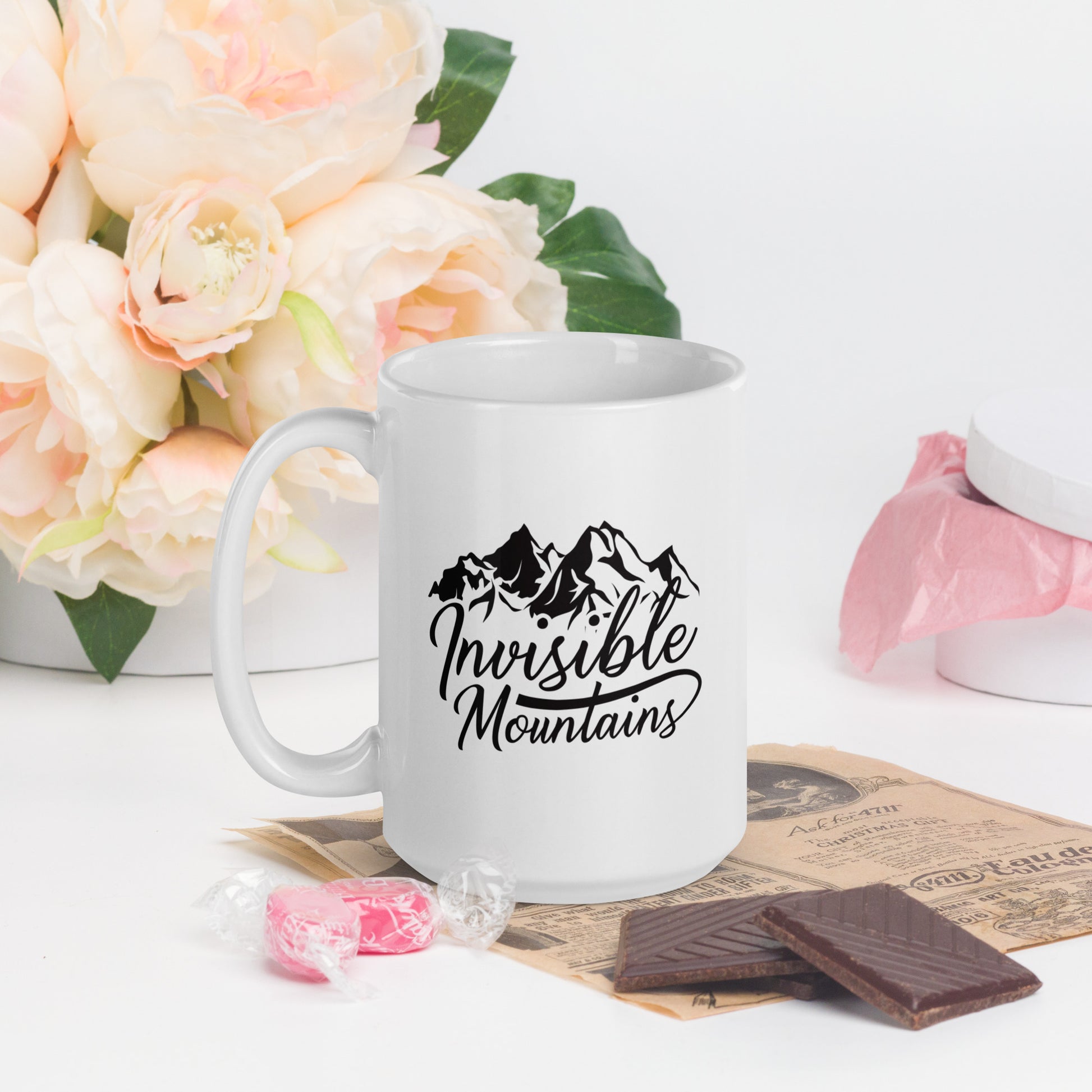 A white coffee mug with the Invisible Mountains Logo. The Invisible Mountains Logo shows the words Invisible Mountain written in cursive under a stylized mountain range 