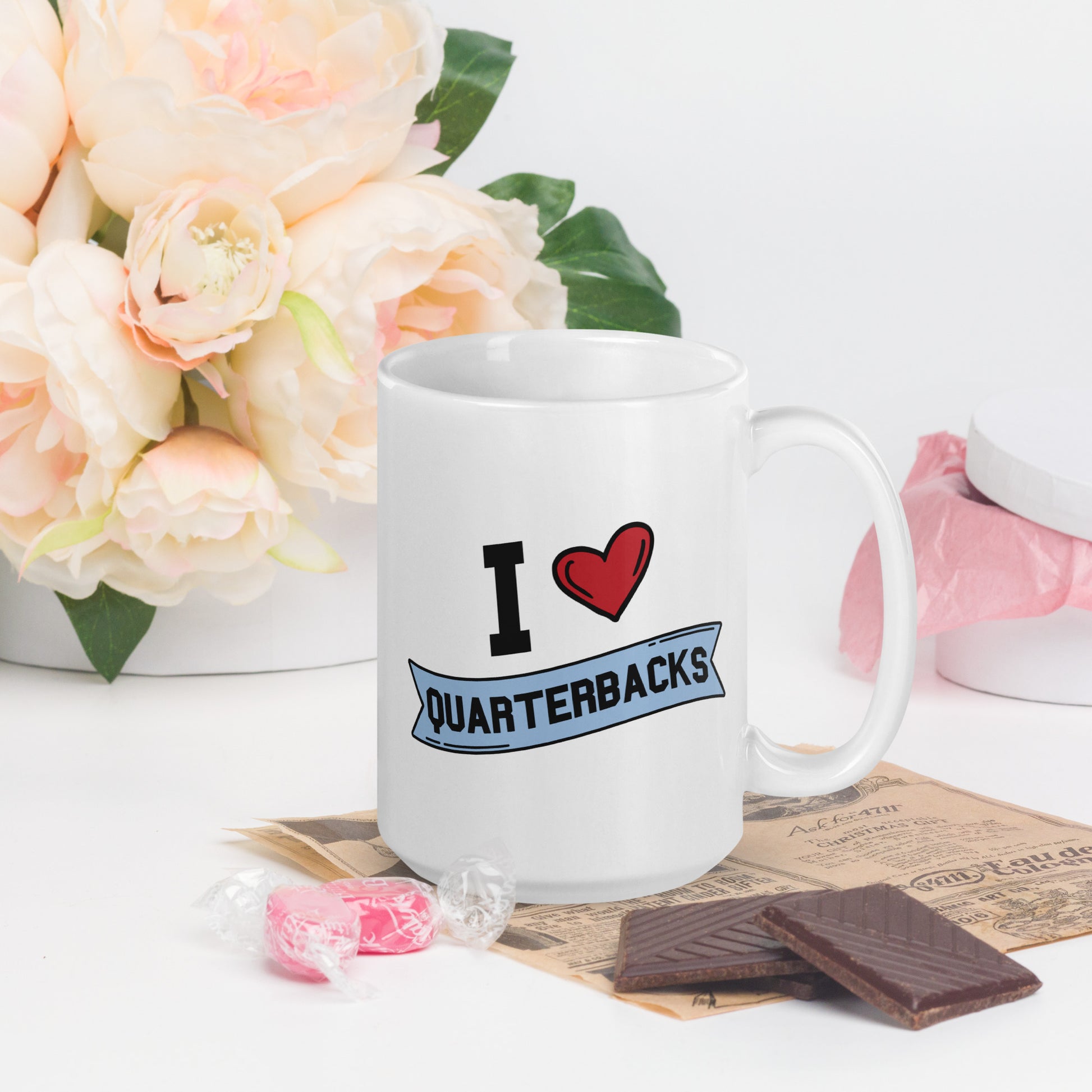 A white mug that reads I Heart Quarterbacks, with a large heart logo. Quarterbacks is in a blue banner 