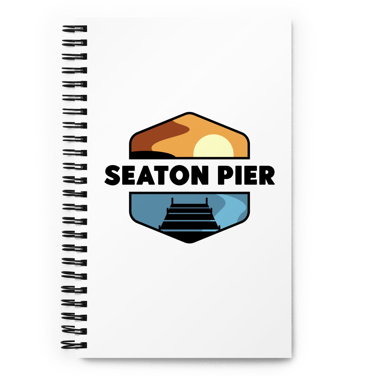 a notebook with the Seaton Pier logo on the cover. The Seaton pier logo features the words Seaton Pier separating the sun and the ocean, with a dark pier on the water