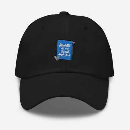 a black cap with the Beckett logo. The Beckett Logo is a blue book with the words Beckett is my book Boyfriend in cursive, with hearts around the book. 