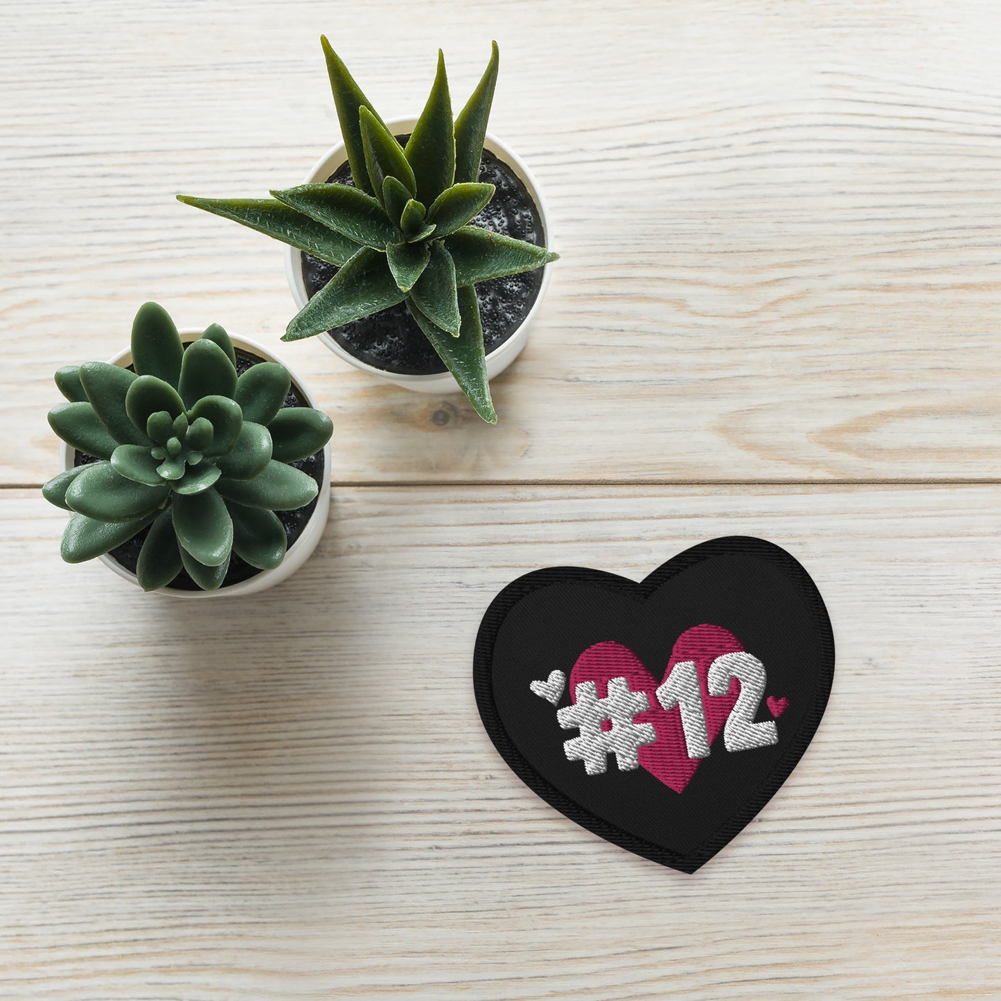 a black heart patch with the I Heart #12 Logo. The Number 12 Logo is a large pink heart with #12 in black written over the heart.