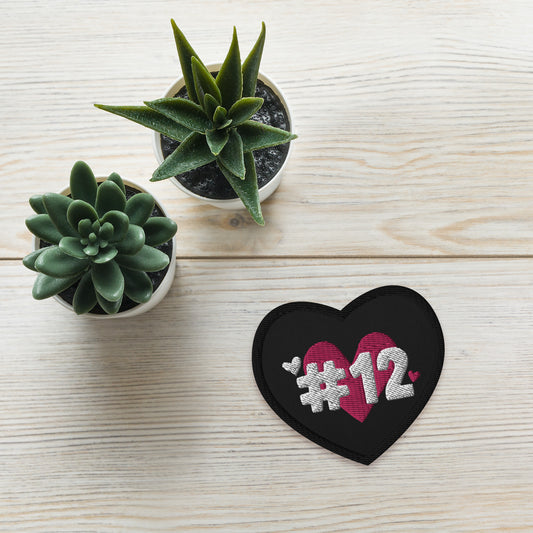 a black heart patch with the I Heart #12 Logo. The Number 12 Logo is a large pink heart with #12 in black written over the heart.