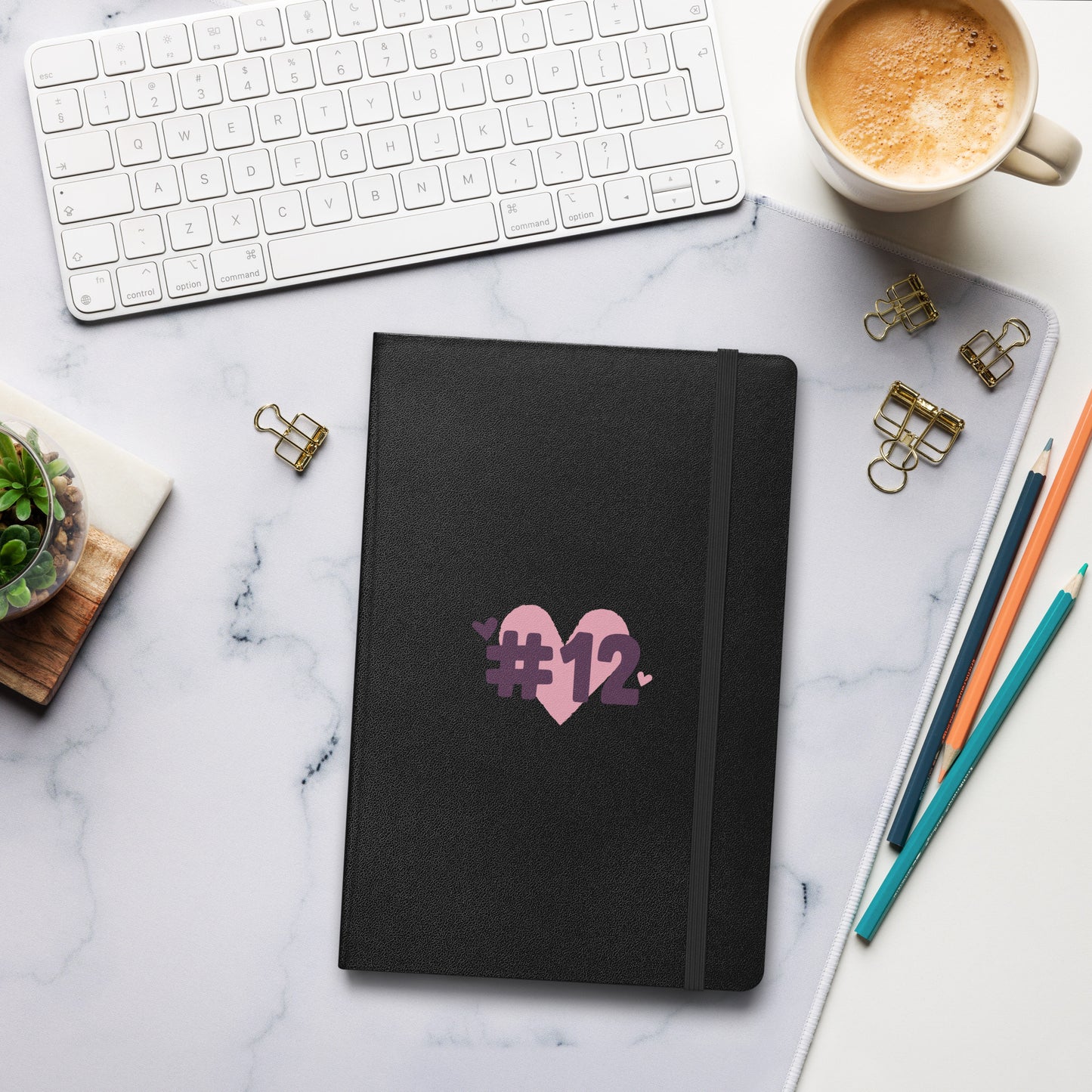 a black notebook with the I Heart #12 Logo. The Number 12 Logo is a large pink heart with #12 in black written over the heart.