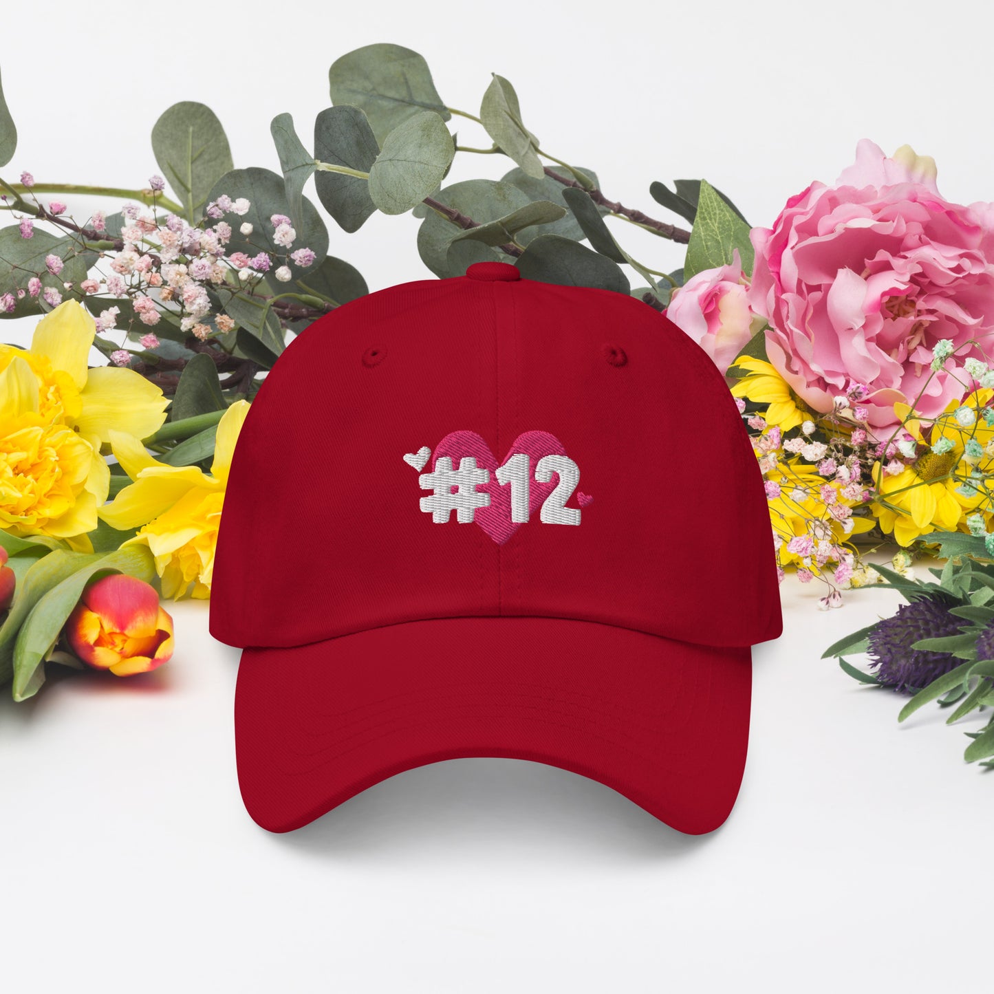 A cranberry cap with the I Heart #12 Logo. The Number 12 Logo is a large pink heart with #12 in black written over the heart.