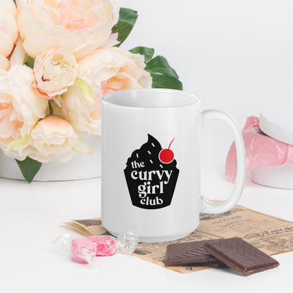 A white coffee mug featuring a black cupcake logo, with white words inside that read "the Curvy Girl Club"