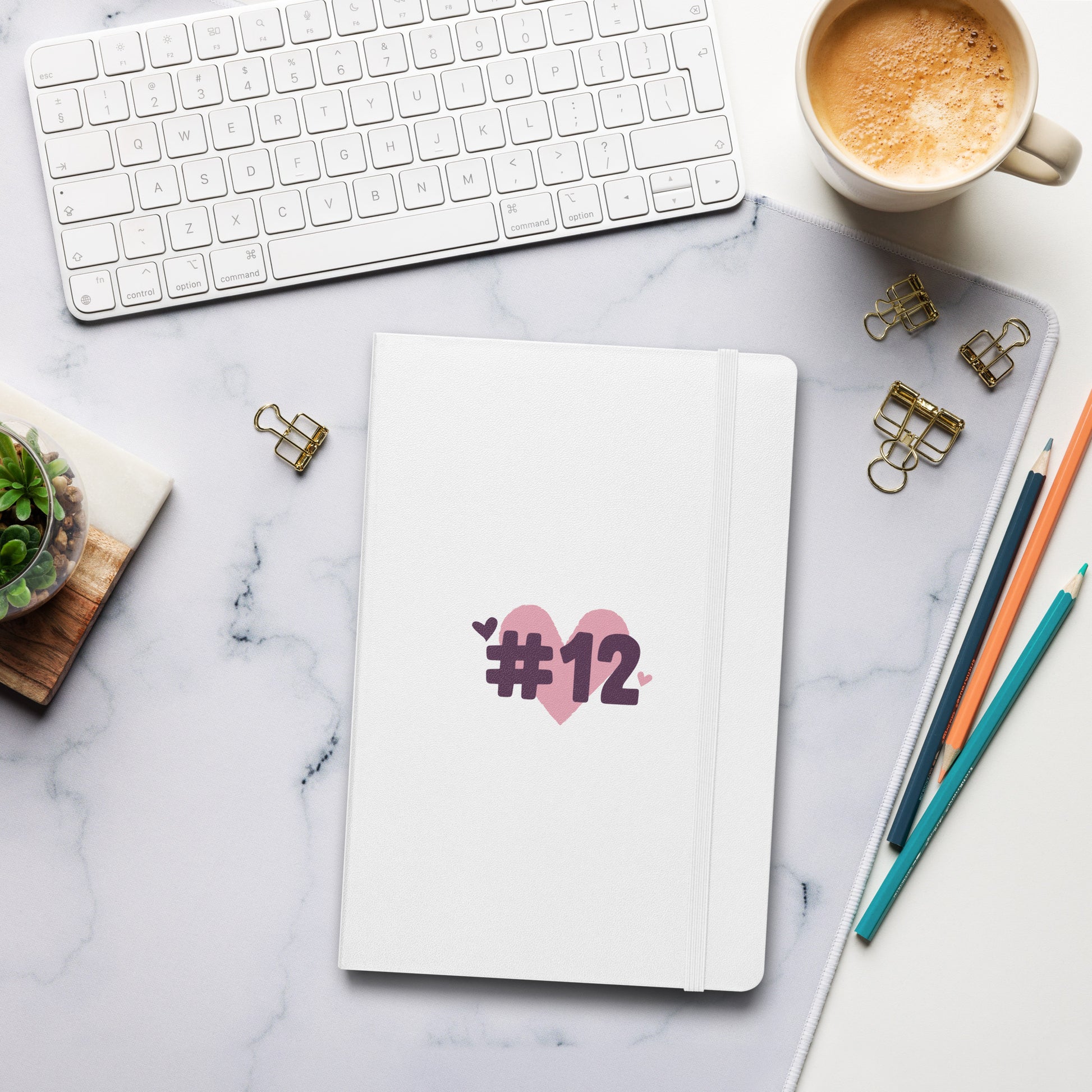 a hardcover notebook with the I Heart #12 Logo. The Number 12 Logo is a large pink heart with #12 in black written over the heart.