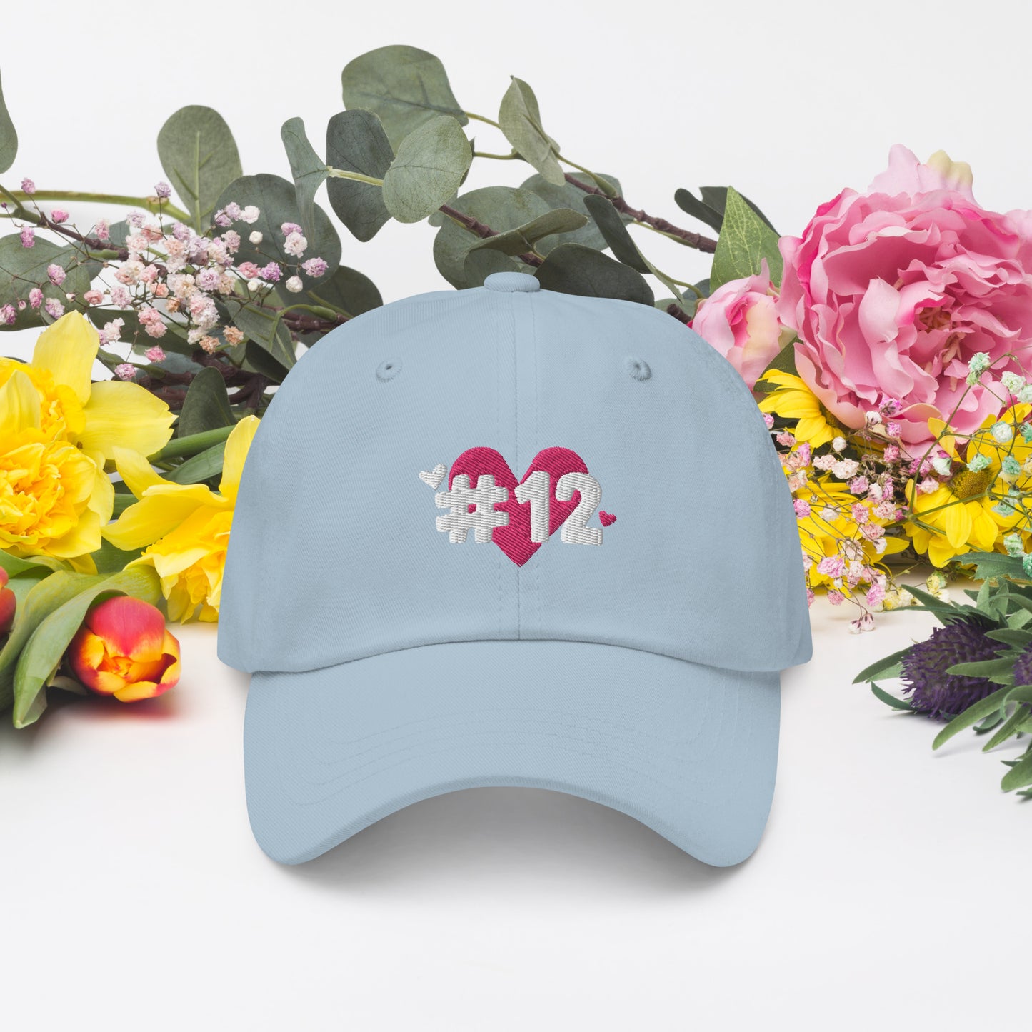 a light blue cap with the I Heart #12 Logo. The Number 12 Logo is a large pink heart with #12 in black written over the heart.