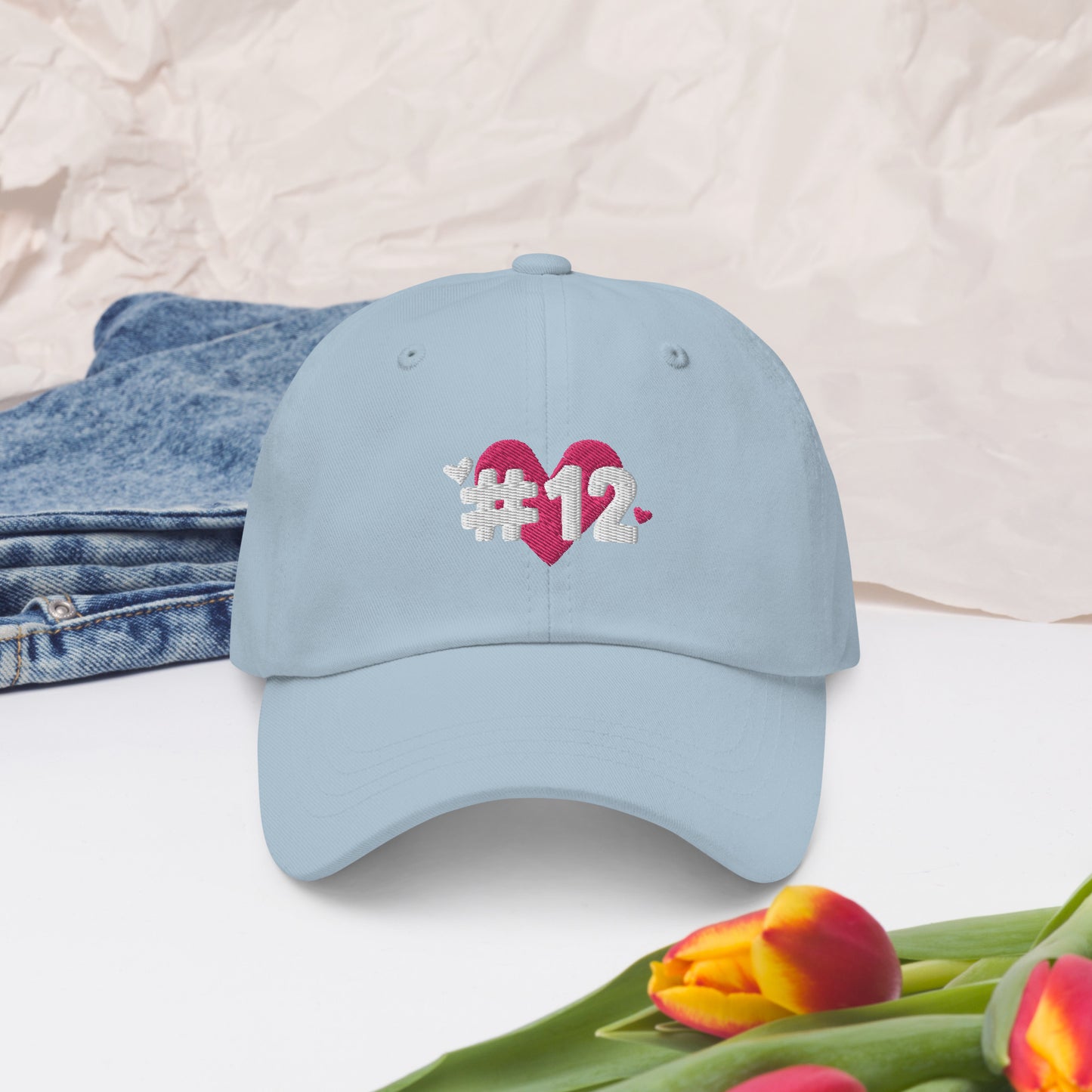 a light blue cap with the I Heart #12 Logo. The Number 12 Logo is a large pink heart with #12 in black written over the heart.