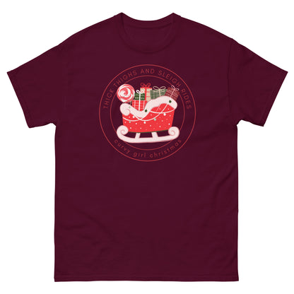 a maroon t-shirt with the Curvy Girl Christmas Sleigh Logo. The logo is a red fluffy sleigh filled with presents, with red lettering circling around that reads Thick Thighs and Sleigh Rides, as well as curvy Girl Christmas