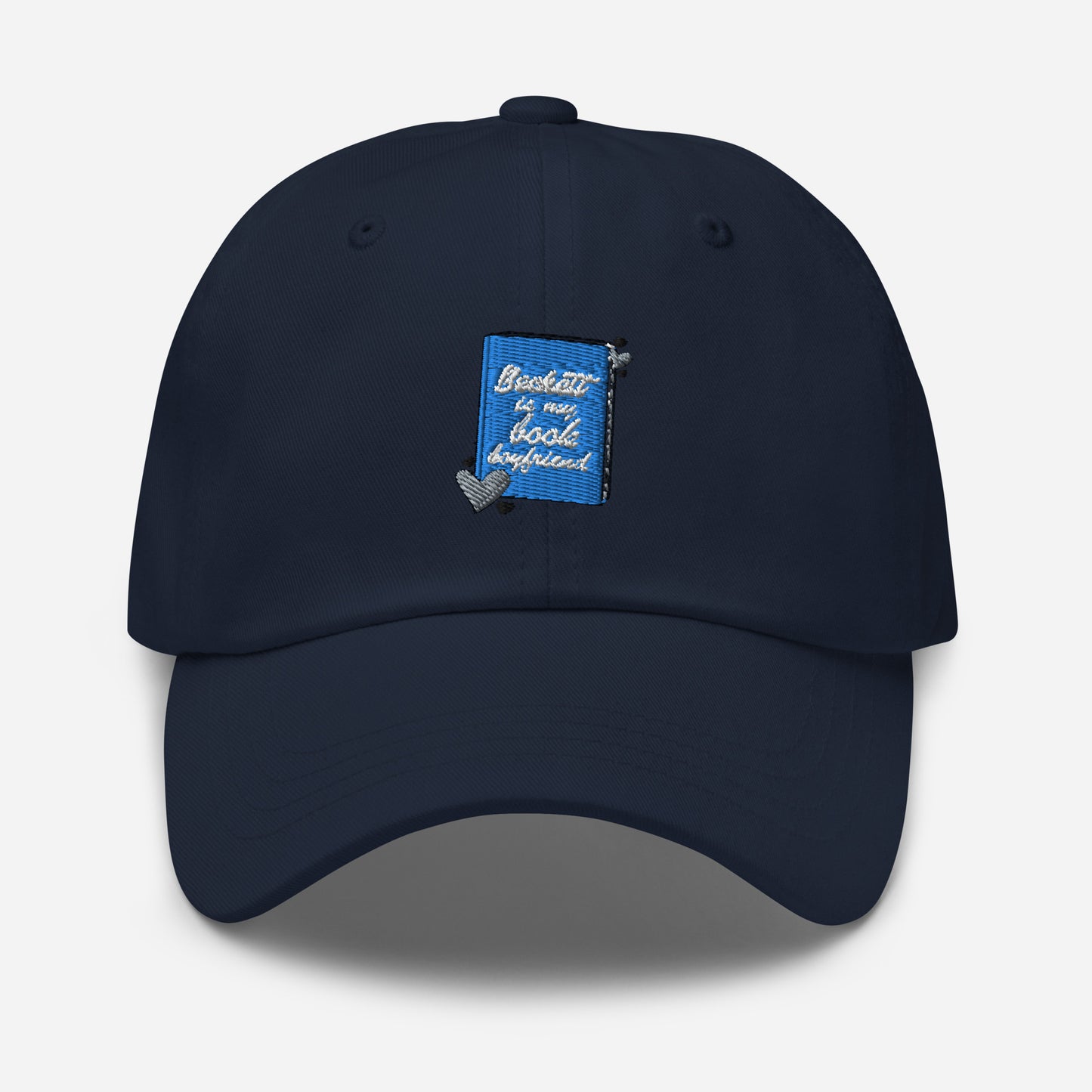 a navy cap with the Beckett logo. The Beckett Logo is a blue book with the words Beckett is my book Boyfriend in cursive, with hearts around the book. 