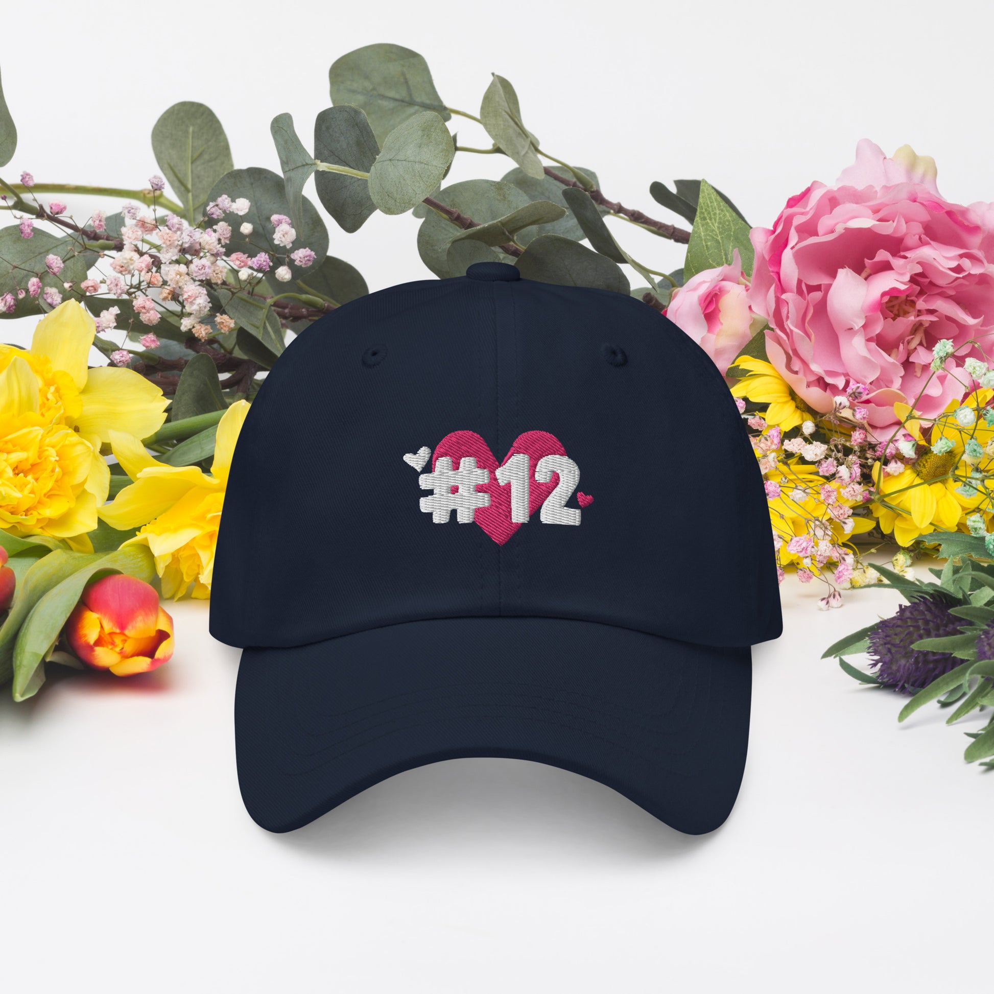 a navy cap with the I Heart #12 Logo. The Number 12 Logo is a large pink heart with #12 in black written over the heart.