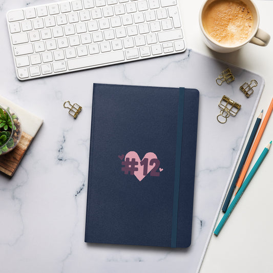 a navy notebook with the I Heart #12 Logo. The Number 12 Logo is a large pink heart with #12 in black written over the heart.