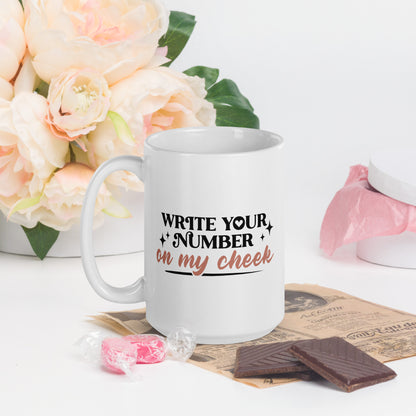 A white coffee mug that reads Write Your number in my cheek in black print and golden cursive
