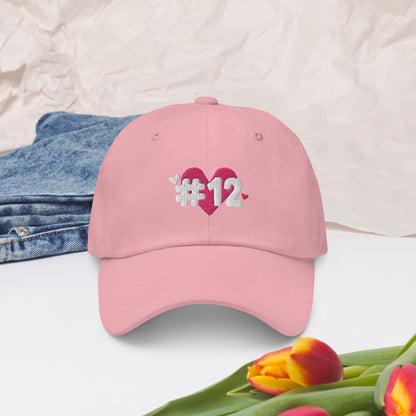 a pink cap with the I Heart #12 Logo. The Number 12 Logo is a large pink heart with #12 in black written over the heart.