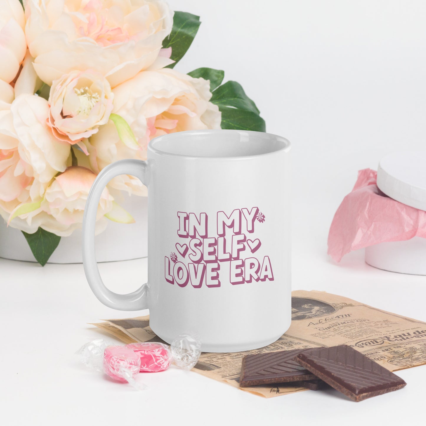 A white mug that reads "In my Self Love Era" in pink bubble lettering, with heart designs